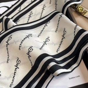 Detail eines eleganten schwarz-weiß gestreiften Seidenschals mit Buchstabendruck auf Tasche