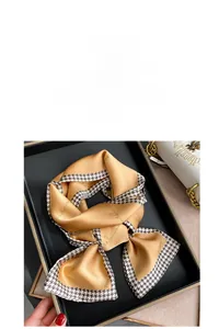 Close-up of champagne satin scarf with houndstooth edge and cursive letters in a gift box