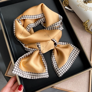 Detail of champagne gold silk scarf with houndstooth and cursive text on black tray