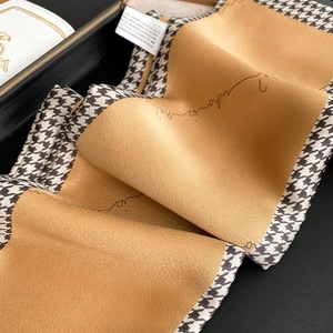 Close-up of houndstooth and camel scarf with elegant handwritten script and care label