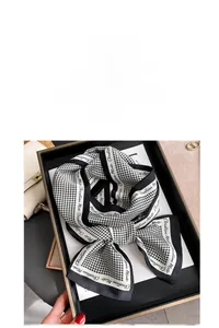 Detail of houndstooth silk scarf with brand text and sleek black border on a tray