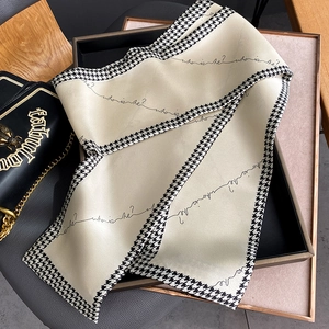 Detail of a beige silk scarf with houndstooth borders and cursive text on a tray