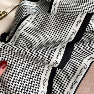 Detail of houndstooth silk scarf tied on a beige leather bag showing premium smooth texture