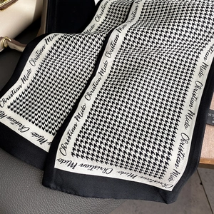 Detailed macro view of black and white houndstooth silk scarf with elegant brand lettering
