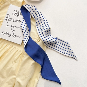Détail d'un foulard en soie réversible bleu roi et à pois sur un vêtement jaune