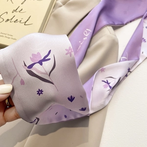 Detail van een elegante lila zijden twilly sjaal met bloemen op een beige blazer