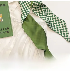 Detail shot of green checkered silk scarf on a white textured dress with prop book