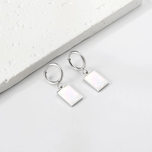 Macro shot of rectangular white shell earrings with polished silver hoops and pearl inlay