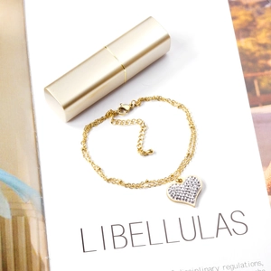 Détail d'une chaîne double dorée avec pendentif cœur pavé de strass blancs brillants