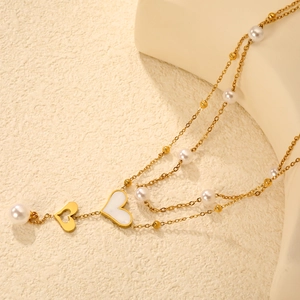 French style double-layered gold heart necklace with white pearls on a textured background