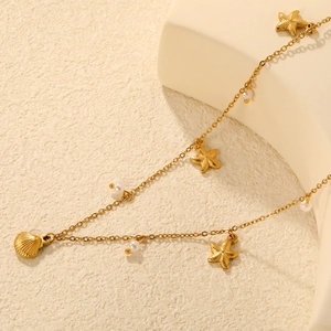 Elegant gold starfish and seashell necklace with pearls on a sandy textured background