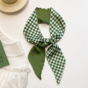 Detail of green and white checkered silk scarf tied in a bow on a white textured background