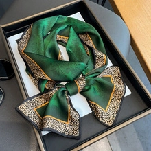Detailed close-up of emerald green silk scarf with golden vintage baroque pattern