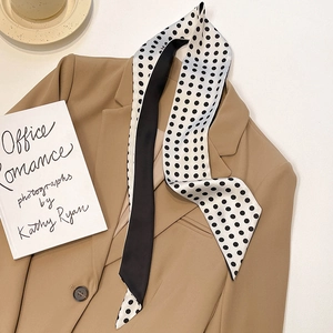Close-up of elegant black and white polka dot silk scarf draped on a khaki blazer collar