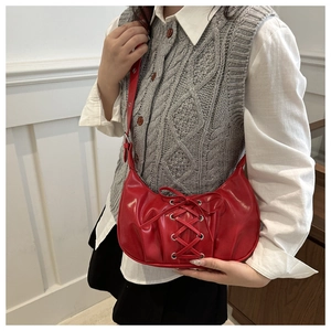 Gros plan d'un sac d'épaule en cuir verni rouge avec rubans croisés et œillets métalliques
