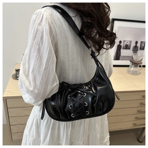 Détail du sac en cuir brillant noir avec rubans croisés porté comme sac sous le bras