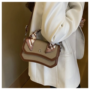 Detail of woven straw crossbody bag with brown leather trim and silk scarf wrapped handle