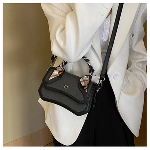 Close-up of black textured handbag with wave flap, golden D charm, and printed silk scarf