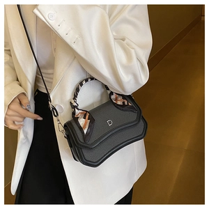 Detail view of black textured leather bag featuring a silver D-ring and silk scarf handle