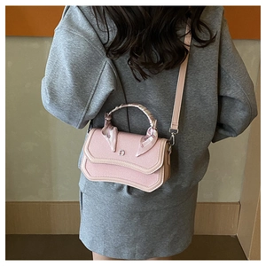 Detail view of pink crossbody bag with curved bottom, scarf handle, and metal D logo