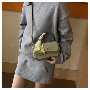 Close-up of light green woven crossbody bag featuring a metal D-logo and floral silk scarf