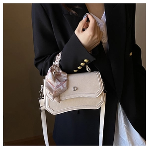 Detail of cream woven shoulder bag with D-shaped metal buckle and silk scarf handle decor