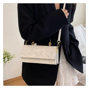 Detail showing 3D butterfly lace embroidery and gold metal chain on beige crossbody bag