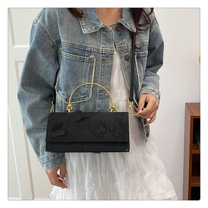 Detail of black lace crossbody bag featuring 3D butterfly embroidery and gold metal handles