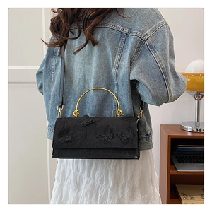 Detailed view of black handbag with 3D butterfly appliques and golden metal handle
