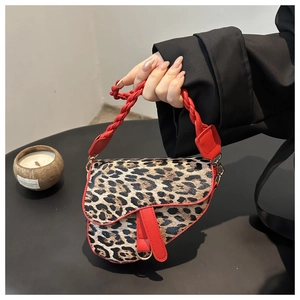 Détail du sac selle léopard avec garniture en cuir rouge et texture de poignée tressée