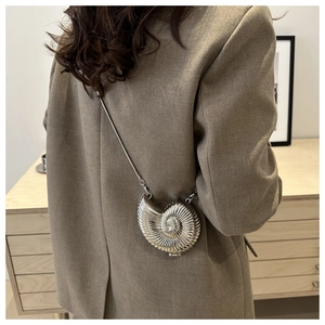 Detail of silver shell-shaped metallic crossbody bag worn by a model in casual attire