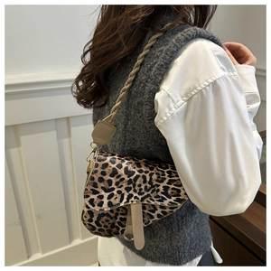 Détail du sac selle léopard montrant la bandoulière tissée et les ferrures métalliques