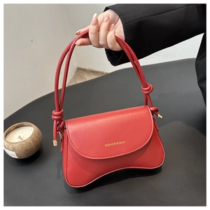 Detail of red matte leather handbag featuring unique wavy base and rope handle with knot