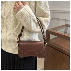 Detail of dark brown leather shoulder bag featuring gold lettering and knotted strap design