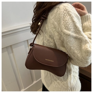 Brown matte leather shoulder bag with gold lettering shown on white knit sweater