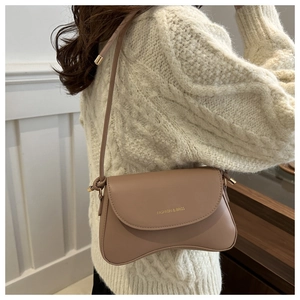 Detail of a khaki curved shoulder bag with gold hardware worn on a white sweater