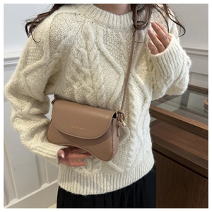 Detail shot of camel saddle bag with curved bottom on white knit sweater