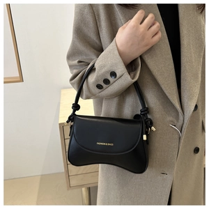 Detail of black leather crossbody bag with gold logo on a model in a beige suit