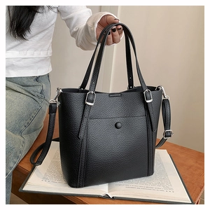 Close-up of black lychee grain leather tote with silver buckles on a wooden desk