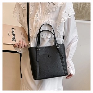Detail of black pebbled leather tote bag with silver hardware on a white lace dress