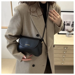 Close-up of black matte leather saddle bag worn by model with gold logo detail