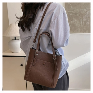 Detail view of dark brown pebbled leather tote bag worn as a shoulder bag on a model