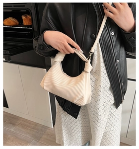 Détail du sac plissé blanc crème avec poignée nouée et finitions métalliques dorées élégantes