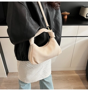 Détail du sac hobo plissé beige porté par un mannequin dans un décor minimaliste