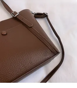 Macro shot of dark brown lychee leather texture and silver buckle on a tote bag