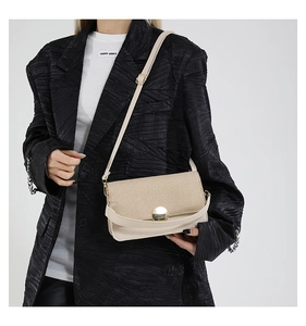 Detail of a beige woven leather crossbody bag with a round gold buckle on a model