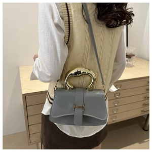 Detailansicht der grauen Box-Tasche mit goldenem Flüssigmetallgriff und H-Verschluss-Detail