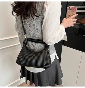 Détail d'un sac noir plissé avec poignée nouée porté par un modèle dans un décor moderne