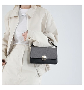 Detail of a textured black leather crossbody bag with a round gold buckle on a model