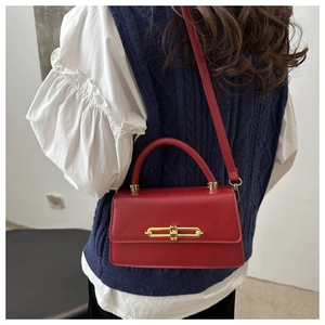Detail of red leather crossbody bag with gold lock buckle and top handle on a model